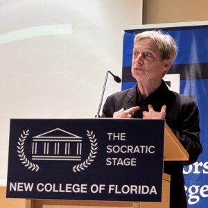 Butler speaks while standing behind a podium with the text "The Socratic Stage" and "New College of Florida."