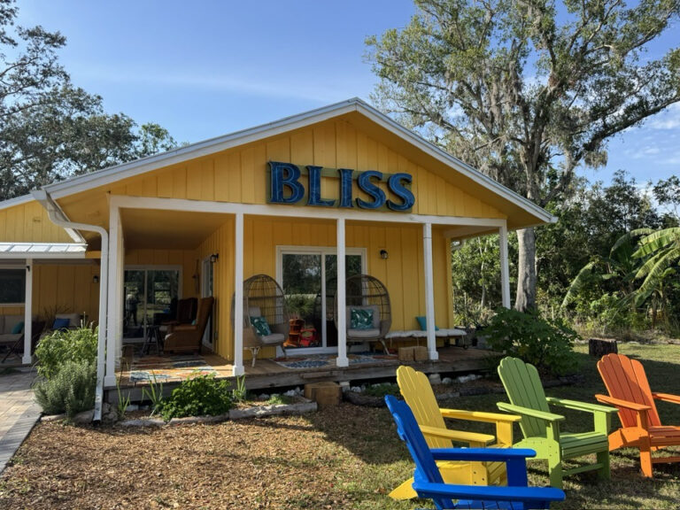 Colorful lawn chairs in front of a yellow house with a blue sign that reads "BLISS".