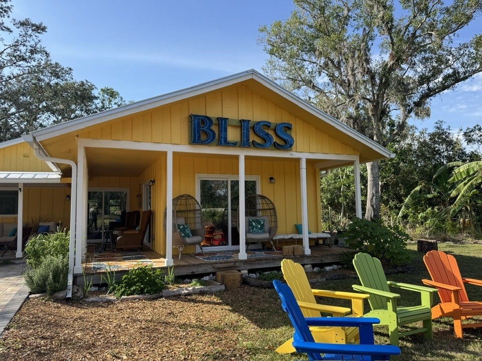 Colorful lawn chairs in front of a yellow house with a blue sign that reads "BLISS".