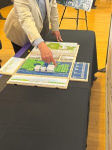 An person whose head is out of frame points at part of a scale model of the proposed performing arts center.