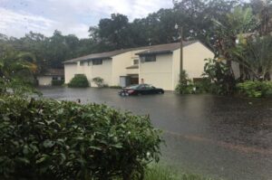 A flooded home with a partially-submerged car parked out front.