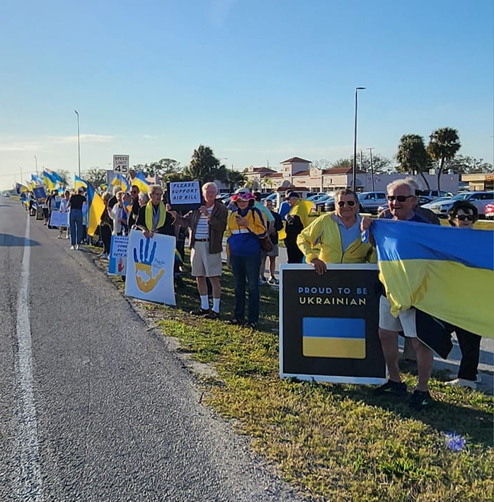 Protesters along the side of the road hold signs and flags in support of Ukraine.