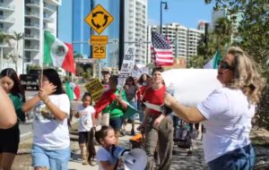 Protestors carry signs and wear shirts in support of immigrants. Someone carries a Mexican flag.