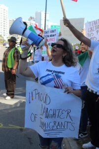 A protestor holds up a megaphone and a sign that reads "Proud daughter of immigrants."