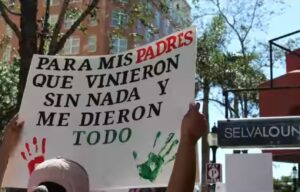 Protestor holding a sign that reads "Para mis padres que vinieron sin nada y me dieron todo."