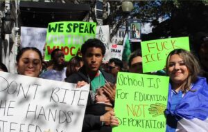 Protestors hold signs with pro-immigrant messages including "We speak for those who can't," "Fuck ICE," "Don't bite the hands that feed you," and "School is for education NOT deportation."