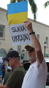 A protester holds a sign with the Ukrainian flag and the text "Slava Ukraini."