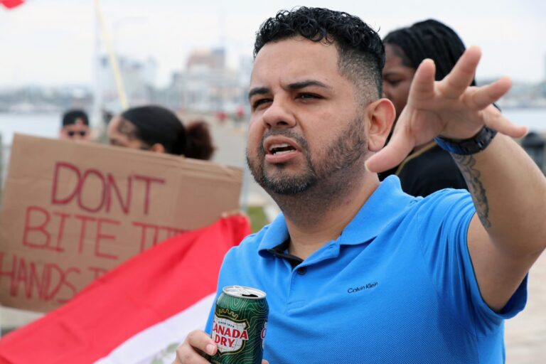 Close-up of Junior Salazar passionately addressing a crowd. A partially obscured sign behind him reads "Don't bite the hands"