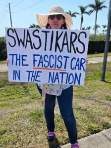 A protester holds up a sign that reads "Swastikars: the fascist car in the nation."