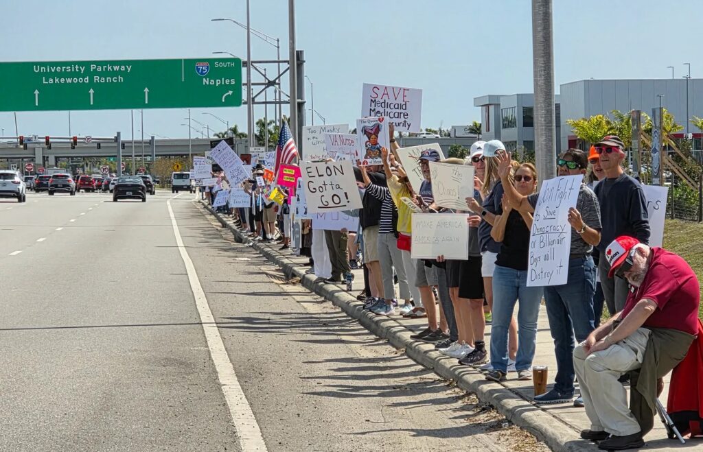 A long line of anti-Musk protesters on the sidewalk along University Parkway.