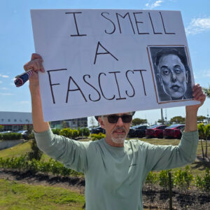 A protester holds up a sign that reads "I smell a fascist" accompanied by a portrait of Musk.