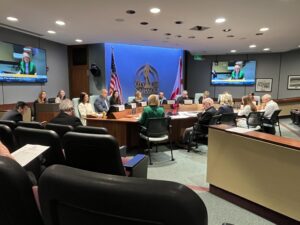 A 13-member committee sits around a conference table. the City of Sarasota logo is on the wall behind them.