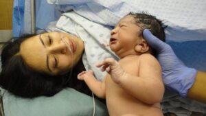 A new parent in a hospital bed looks at their infant child.