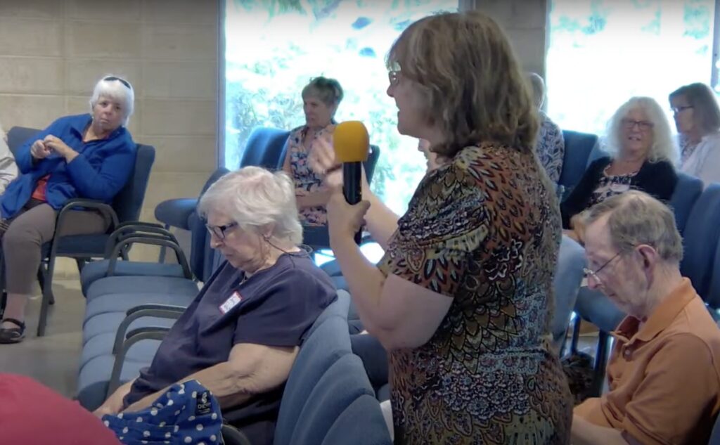 Audience at a forum. One member stands and speaks into a microphone.