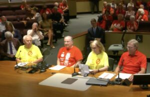 Folks in red and yellow t-shirts review prepared notes at a table before city hall.
