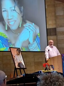 Ed Linehan speaks at a podium with a projected photo of Synia Carroll behind him.