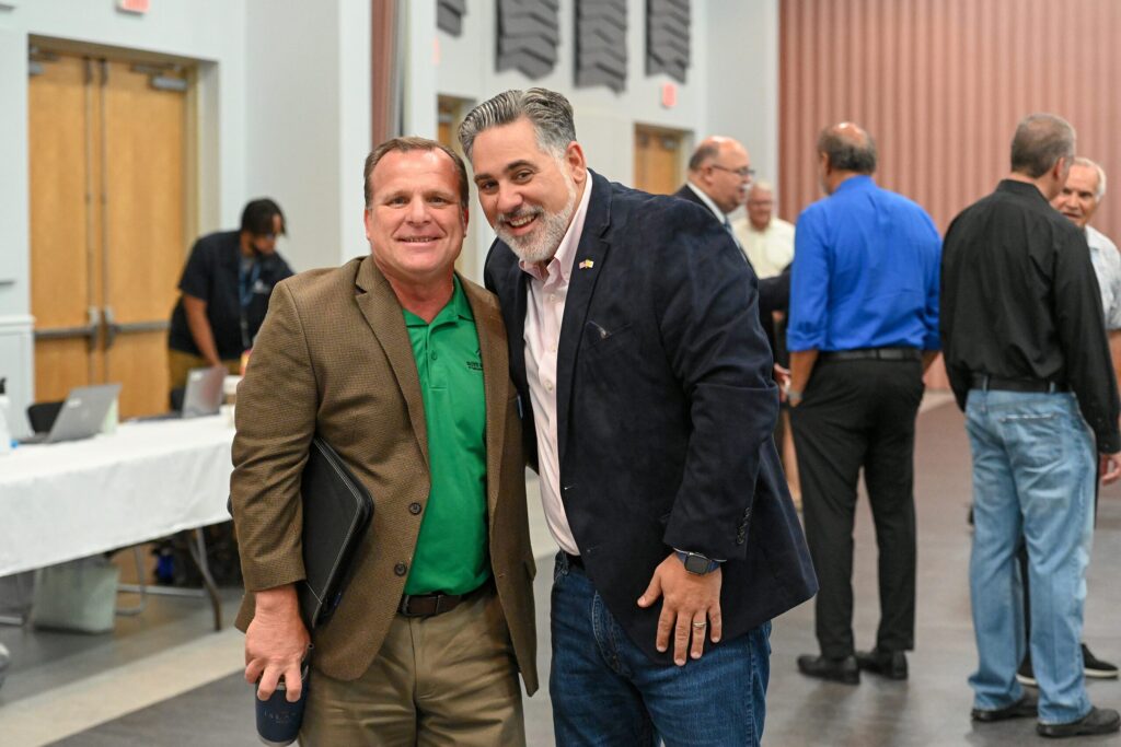 Joe Neunder smiles warmly alongside a representative from Boys & Girls Clubs of Sarasota in a convention hall.