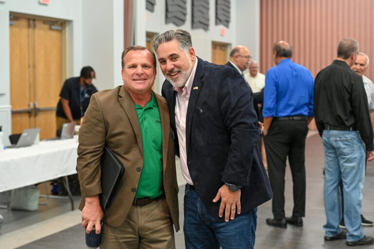 Joe Neunder smiles warmly alongside a representative from Boys & Girls Clubs of Sarasota in a convention hall.