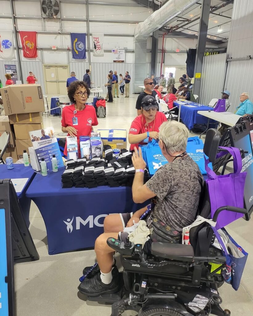 A person in a motorized wheelchair speaks with MCR Health employees at a booth where they're giving away branded merchandise.