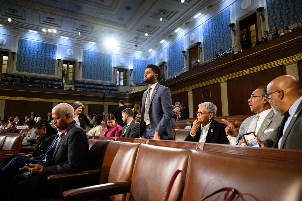 Max Frost standing in the House Chamber. The other representatives are seated.
