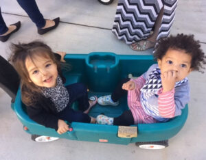 Two children sitting in a wagon, looking up at the camera and smiling.