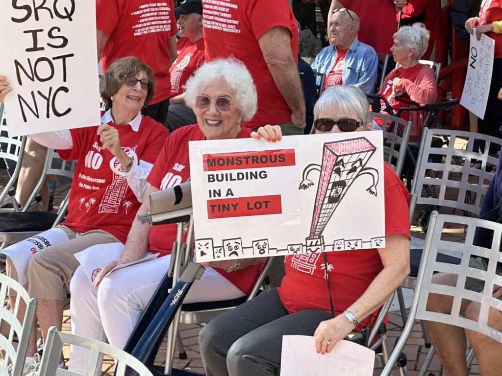 Protesters wearing red t-shirts that say "Say NO To the Skyscraper on Palm Ave" hold protest signs that read "SRQ is not NYC" and "Monstrous building in a tiny lot."