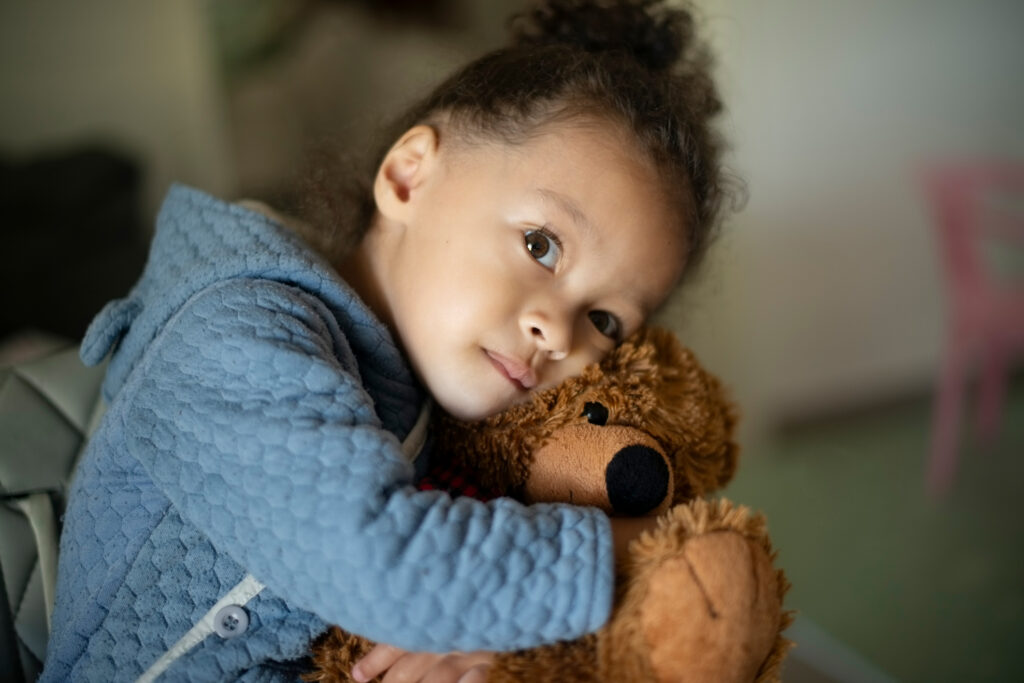 A sad child clutching a stuffed teddy bear.