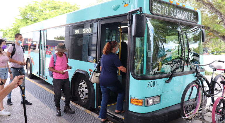 People boarding a bus. The destination indicator reads "99 TO SARASOTA".