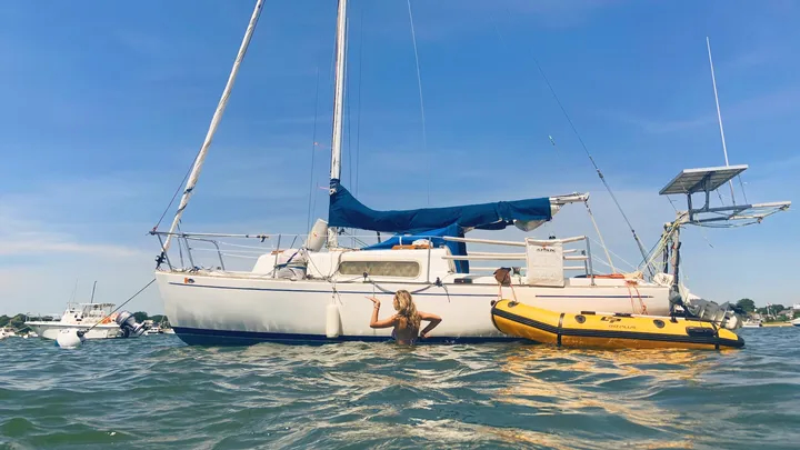 A person in the ocean strikes a pose in front of a boat.