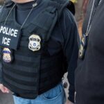 Two ICE officers photographed from the neck down, badges prominently visible.
