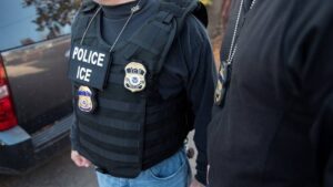 Two ICE officers photographed from the neck down, badges prominently visible.