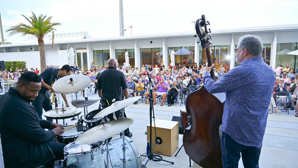 Outdoor photo from behind four jazz performers looking out at the large crowd there to see them.