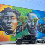 A huge mural depicting Irene and Rev. Lewis Colson on the wall of a building. Abstract floral patterns fill the colorful background. Half of each subject's face is in greyscale.