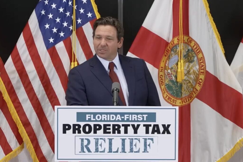 Gov. Ron DeSantis behind a podium labeled "Florida-First Property Tax Relief" and in front of a U.S. flag and a Florida state flag.
