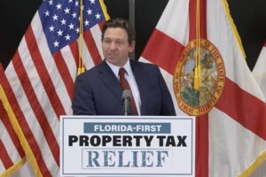 Gov. Ron DeSantis behind a podium labeled "Florida-First Property Tax Relief" and in front of a U.S. flag and a Florida state flag.