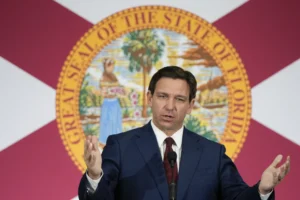 Ron DeSantis gesticulating while speaking in front of a FLorida state flag.