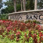 Mixed stone sign that reads "Harrison Ranch" in front of palm trees and behind landscaped foliage.