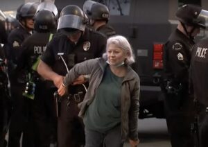 LAPD officers apprehend a protester who wears a resigned expression.