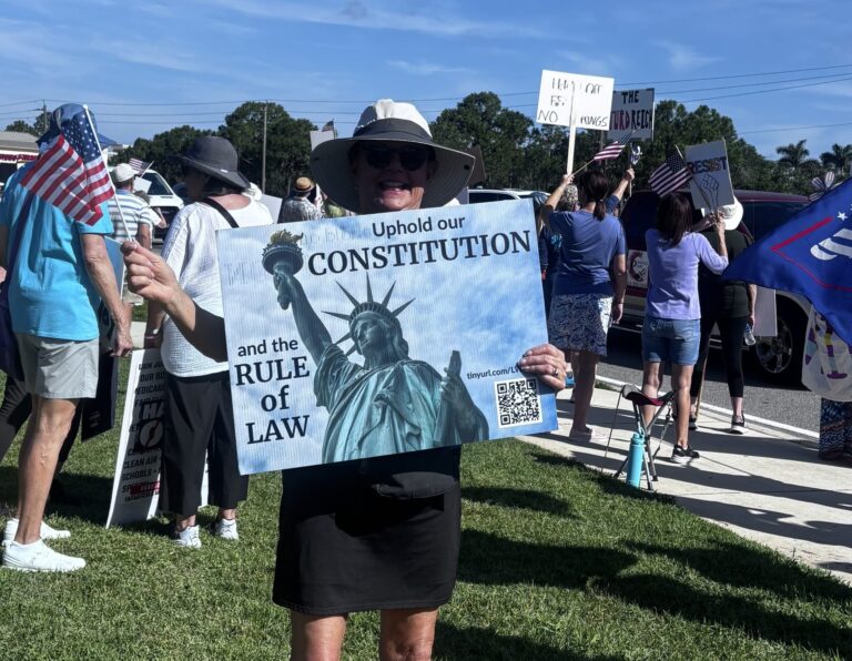 A demonstrator at a protest holds a sign that says "Uphold our constitution and the rule of law" with a photo of the Statue of Liberty." In the background, another demonstrator's handwritten sign reads "The Turd Reich."