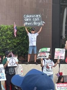 A very young demonstrator holds up a sign that says "Colonizers can't call others illegal!"