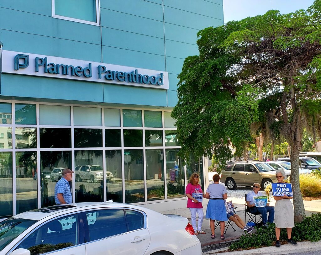 A handful of picketers outside a Planned Parenthood clinic.Some hold signs that read "Pray to end abortion".