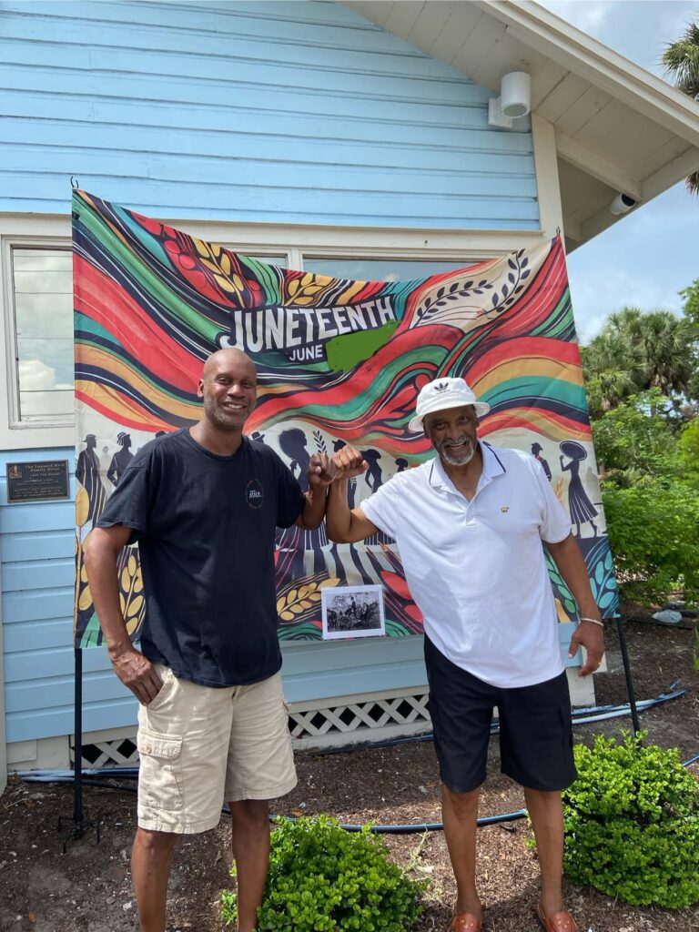 Photo of two people posing proudly in front of a Juneteenth banner.