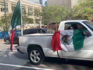 Photo of a white truck. The passenger is holding a Mexican flag out the window.