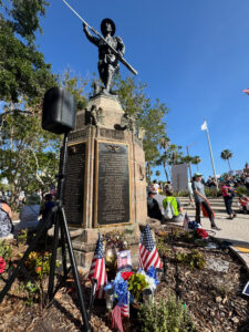 A crowd of demonstrators gathers near a statue of a World War I soldier honoring area veterans.