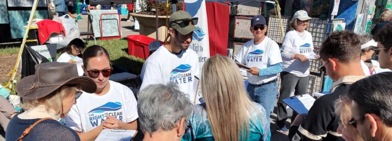 A crowd approaches a group of volunteers wearing T-shirts that say "The Right to Clean Water" at an outdoor convention.