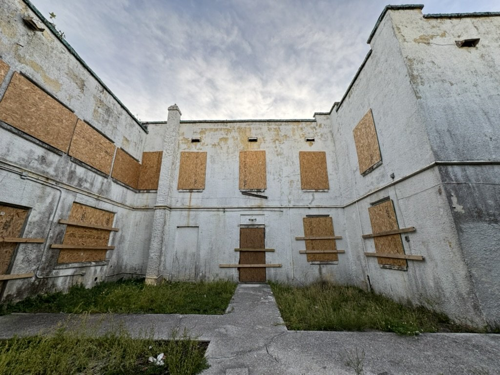 Photo of a dilapidated old building with boarded-up windows, taken from a small courtyard.