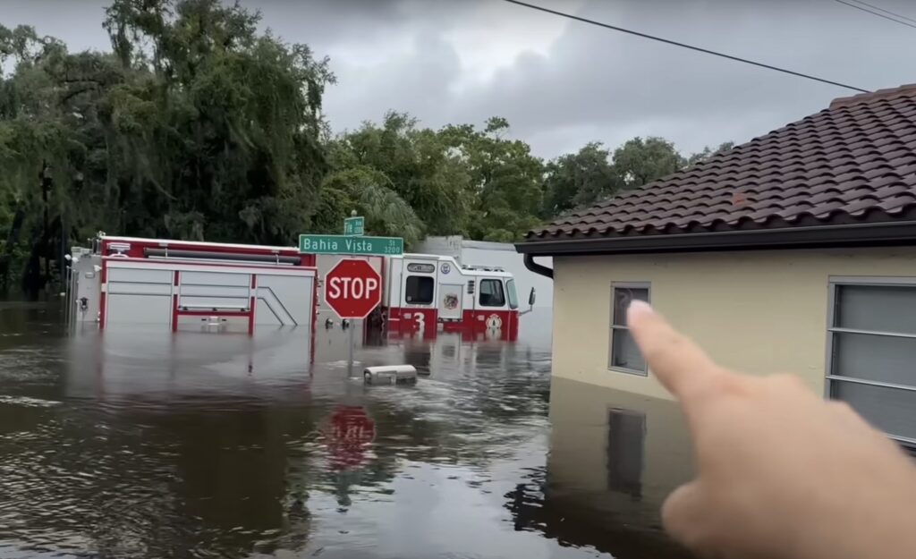 Photo of a firetruck half-submerged by floodwater. The photographer points at the scene.