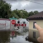 Photo of a firetruck half-submerged by floodwater. The photographer points at the scene.