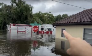 Photo of a firetruck half-submerged by floodwater. The photographer points at the scene.