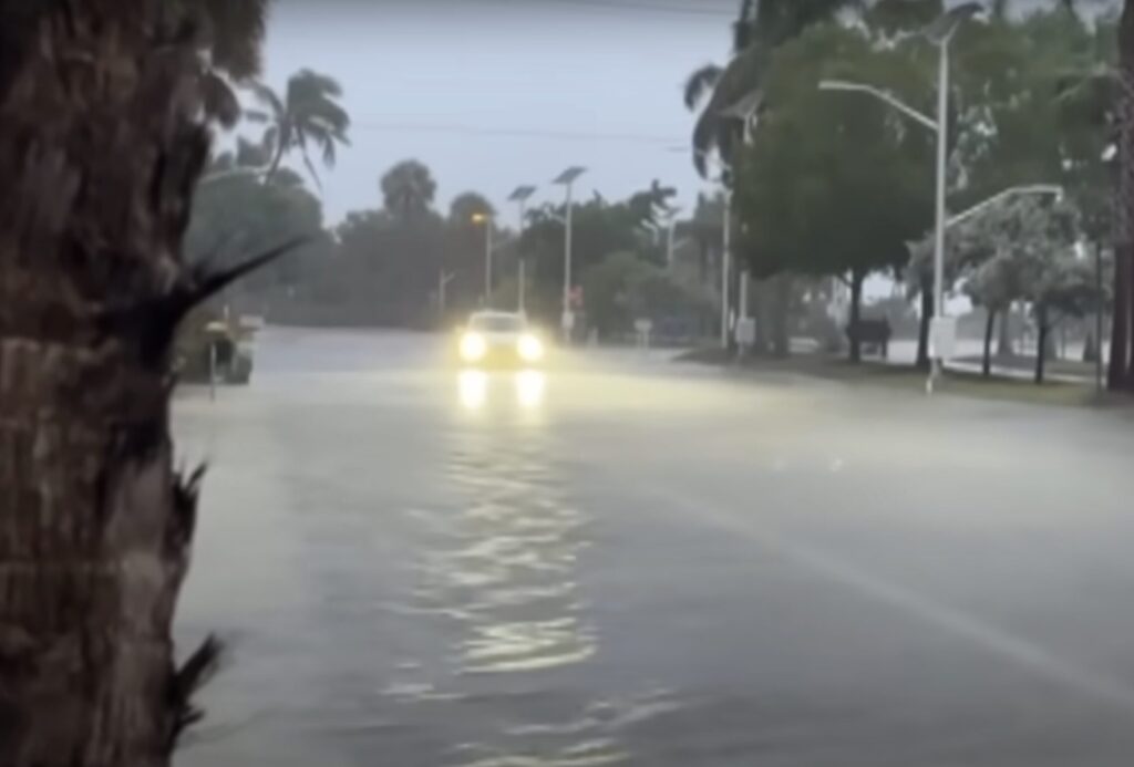 Photo of a car with bright headlights driving on a flooded street.